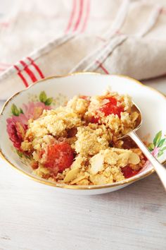 a bowl filled with fruit and crumbs next to a spoon on top of a table