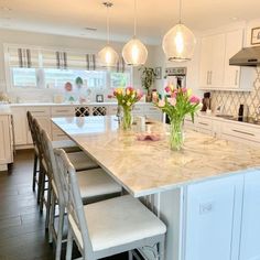 a large kitchen with marble counter tops and white cabinets, along with four stools