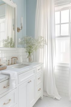 a white bathroom with blue walls and curtains on the windowsill, along with two sinks