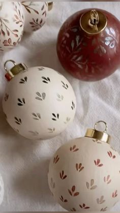 three white and red christmas ornaments on a table cloth with gold trimmings, one in the shape of an ornament