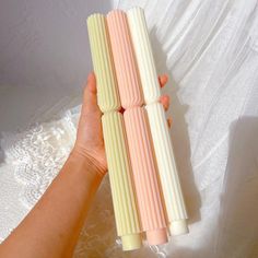 a hand holding three different colored candles on a white tablecloth with lace in the background