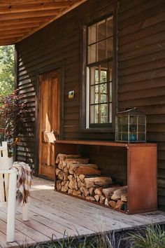 a house with wood stacked on top of it's porch and a table in front of the door