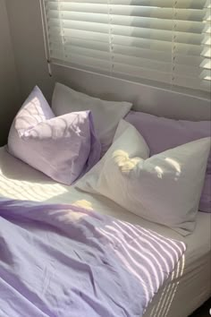 a bed with purple sheets and pillows on top of it in front of a window