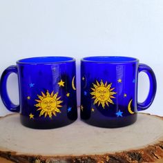 two blue mugs with the sun and moon painted on them sitting on a piece of wood