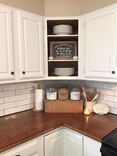 a kitchen with white cabinets and wooden counter tops, including plates on the shelf above the sink