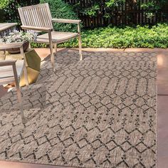 an outdoor area rug with two chairs and a table on the ground in front of some bushes