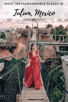 a woman in a red dress walking across a suspension bridge