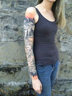 a woman with a tattoo on her arm standing next to a stone wall and looking at the camera