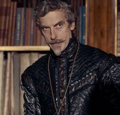 a man wearing a black leather jacket with a moustache on his face in front of bookshelves