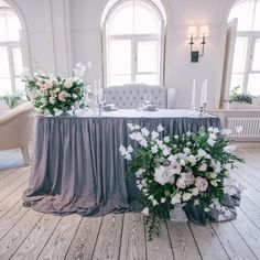 the table is set with white flowers and greenery on it, along with candles