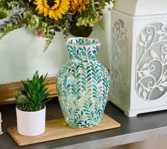 a blue vase sitting on top of a wooden table next to a potted plant