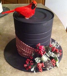 a red bird sitting on top of a black hat with holly and berries around it