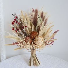 a vase filled with lots of dried flowers on top of a white table covered in lace