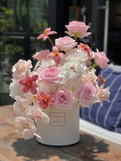 a white vase filled with pink and white flowers on top of a wooden table next to a couch