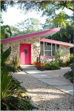 a pink door is in front of a stone house with plants and trees around it