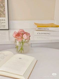 three books are stacked on top of each other near a vase with flowers in it