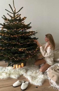 a woman sitting on the floor next to a christmas tree