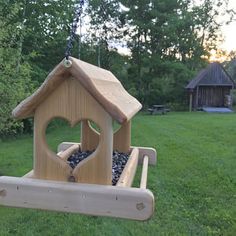 a wooden bird house hanging from a chain in the grass next to a park bench