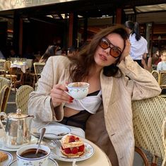 a woman sitting at a table with food in front of her and drinking from a cup