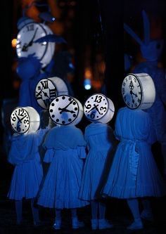 several people in blue dresses with clocks on their heads and hands, all looking at the same time