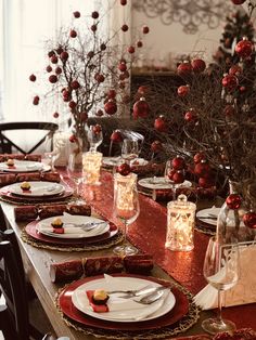 the table is set for christmas dinner with red flowers and silverware, candles and plates