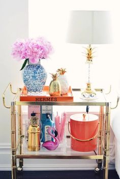 a gold bar cart with pink flowers and other items on it in front of a window