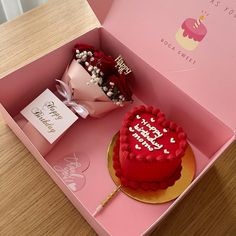 a heart shaped cake in a pink box with a flower on the table next to it