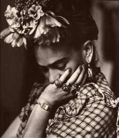 a black and white photo of a woman with flowers in her hair holding her hands to her face