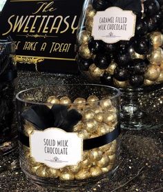 some gold and black balls are in a glass bowl on the counter next to chocolates