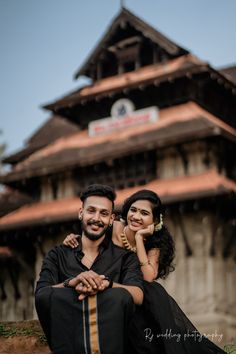 a man and woman sitting on the ground in front of a building