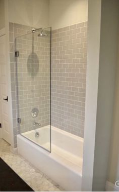 a bath tub sitting next to a white door in a bathroom with gray tile on the walls