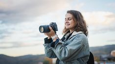 a woman holding a camera up to her face with the sky in the back ground