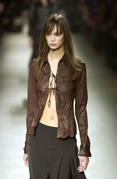 a woman walking down a runway wearing a brown shirt and black skirt with high heels