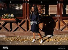 a woman talking on her cell phone while walking down the street in autumn - stock image