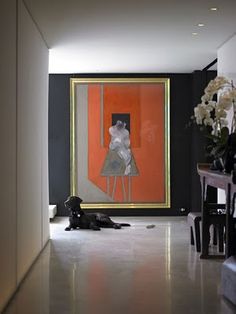 a black dog laying on the floor in front of an orange and white painting with flowers