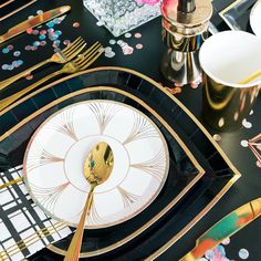 a black and gold place setting with confetti on the plates, napkins and cutlery