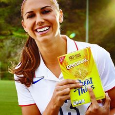 a woman holding a carton of cereal in her right hand and smiling at the camera