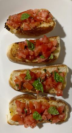 three pieces of bread with tomatoes and basil on them, sitting on a white plate