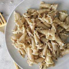 a white plate topped with pasta covered in sauce and seasoning next to a fork