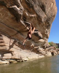 a shirtless man climbing up the side of a cliff next to a body of water