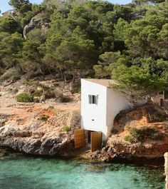 a small white house sitting on top of a cliff next to the ocean and trees