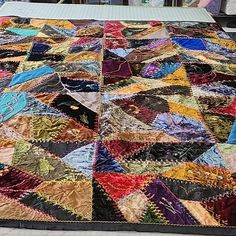 an old quilt is laying on the ground in front of a tablecloth that has been turned into a blanket