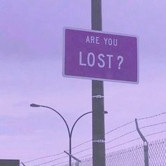 a purple sign that says are you lost? on a pole next to a fence