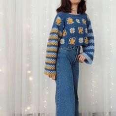 a woman standing in front of a white curtain wearing a blue and yellow knitted sweater