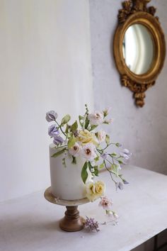 a small white cake with flowers on top sits on a table in front of a mirror