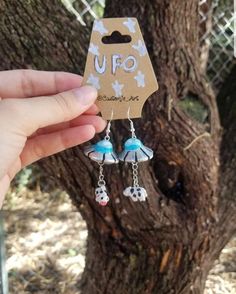 a person holding up a pair of blue and white earrings in front of a tree