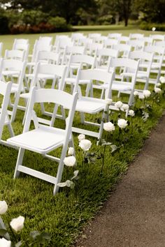 rows of white folding chairs sitting on top of a grass covered field next to flowers