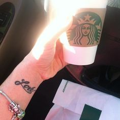 a woman's arm with a tattoo on it and a starbucks cup in her hand