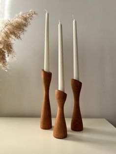 three wooden candlesticks sitting on top of a table next to a dried plant