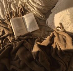 an open book laying on top of a bed covered in blankets and pillows next to a pillow